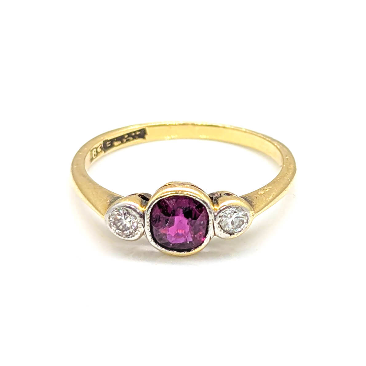 A yellow gold ring featuring a central oval-cut pinkish-purple gemstone flanked by two small round clear stones in a silver-toned setting, shown on a plain white background.