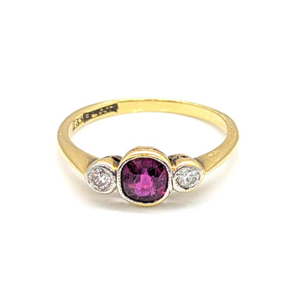 A yellow gold ring featuring a central oval-cut pinkish-purple gemstone flanked by two small round clear stones in a silver-toned setting, shown on a plain white background.